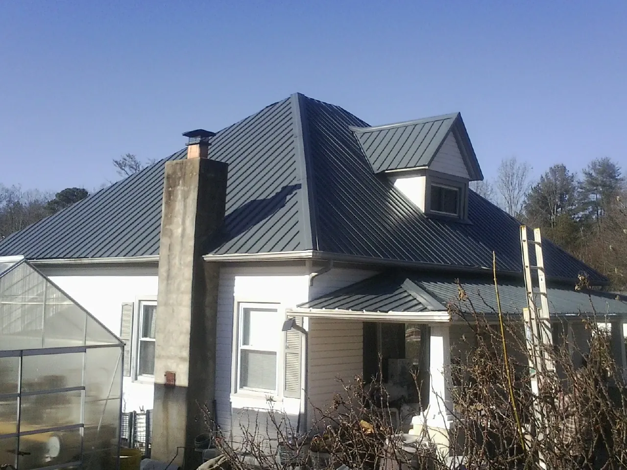 Dark blue standing seam metal roof on a white farmhouse with dormer — Slate & Tile Roof Repair by Roofing Brothers in Otho