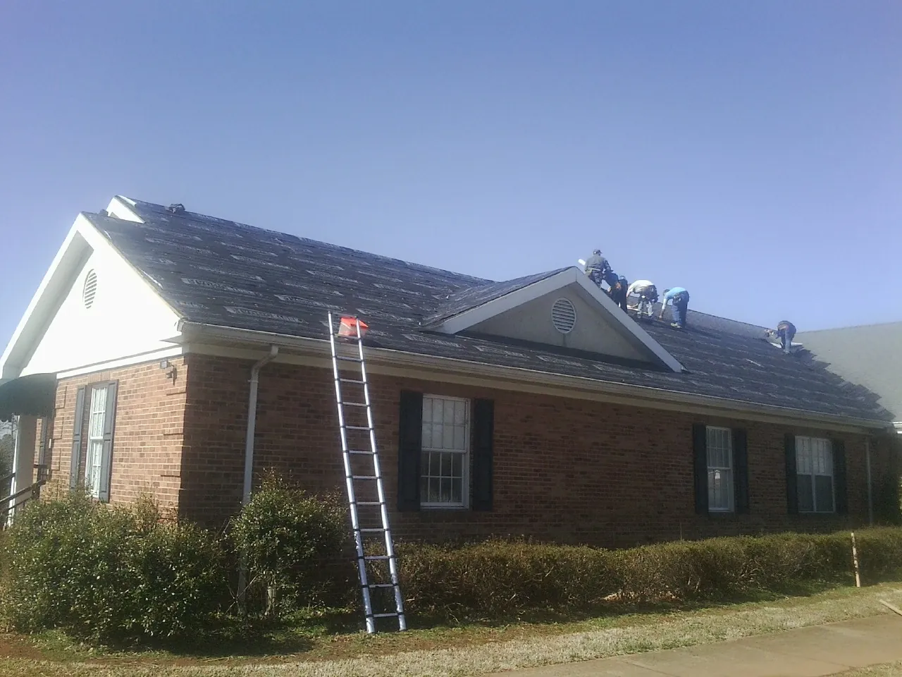 Crew tearing shingles off a brick ranch roof with a ladder set — Emergency Roof Repair work by our crew in Otho