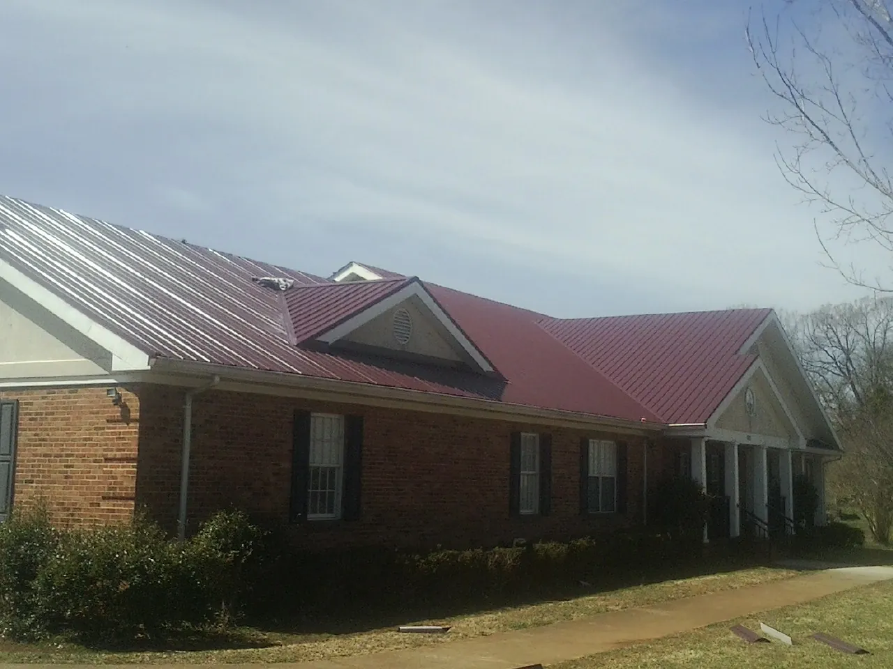Red metal roof with gabled entries on a long brick building, from a Hail Damage Roof Repair job in Otho