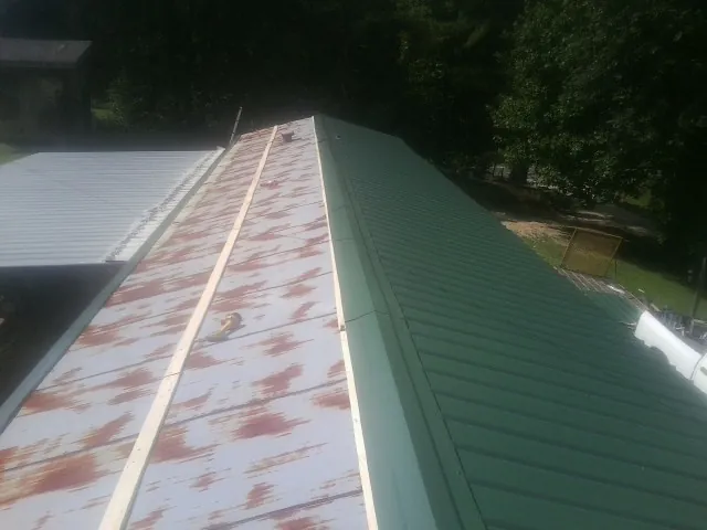 Old rusted panels beside newly installed green metal roofing — Wind Damage Roof Repair by Roofing Brothers in Otho