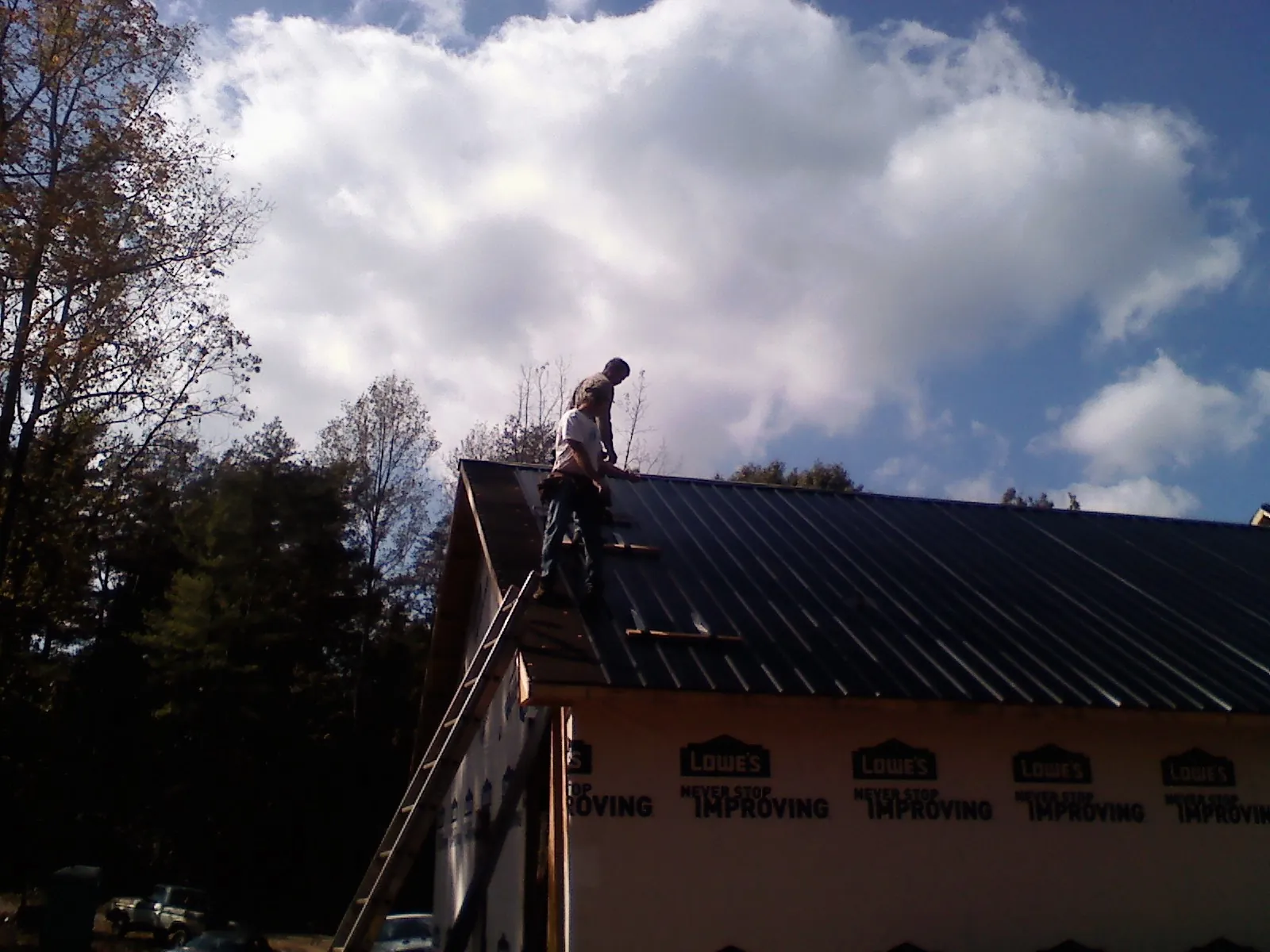 Roofer fastening dark metal panels high against a cloudy sky, from a Roof Inspection job in Otho