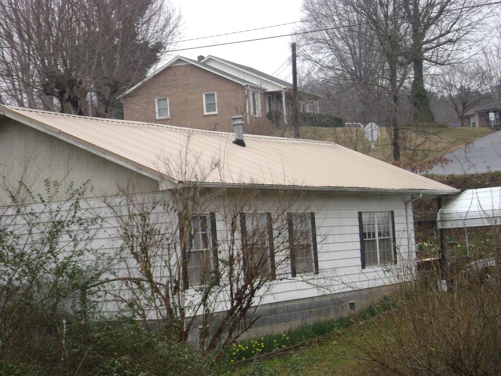 Tan metal roof on a white sided house set into a hillside — Commercial Roofing by Roofing Brothers in Otho